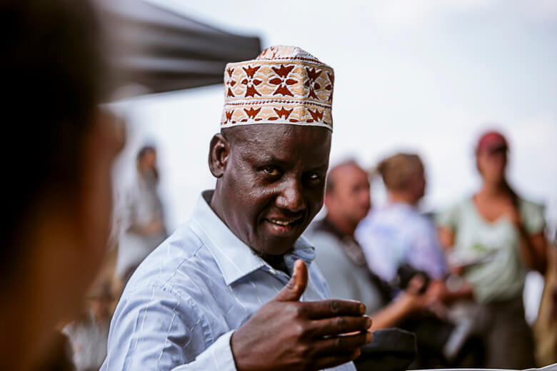 Smiling man in traditional patterned hat giving thumbs up in crowd