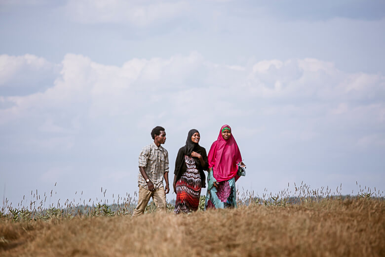 Three people walking together in a grassy field under cloudy sky