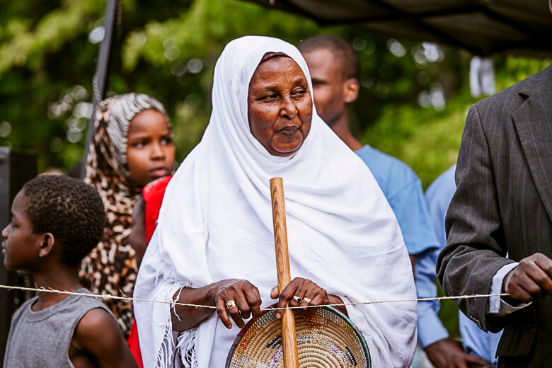 Elderly woman in white hijab holding walking stick and woven basket