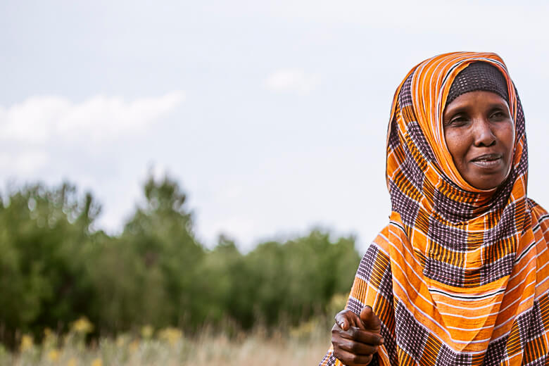 Woman in vibrant orange and brown hijab standing in grassy field
