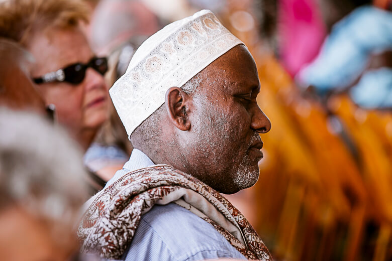 Man in white cap and traditional scarf at a crowded gathering