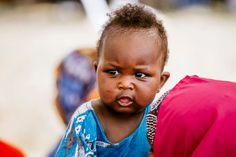 Adorable baby in blue shirt looking directly at camera with curious expression