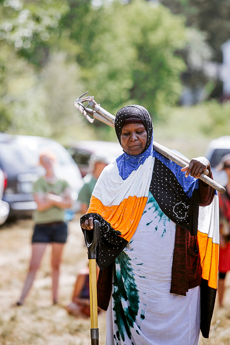 Woman in colorful headscarf carrying tools, standing in outdoor setting