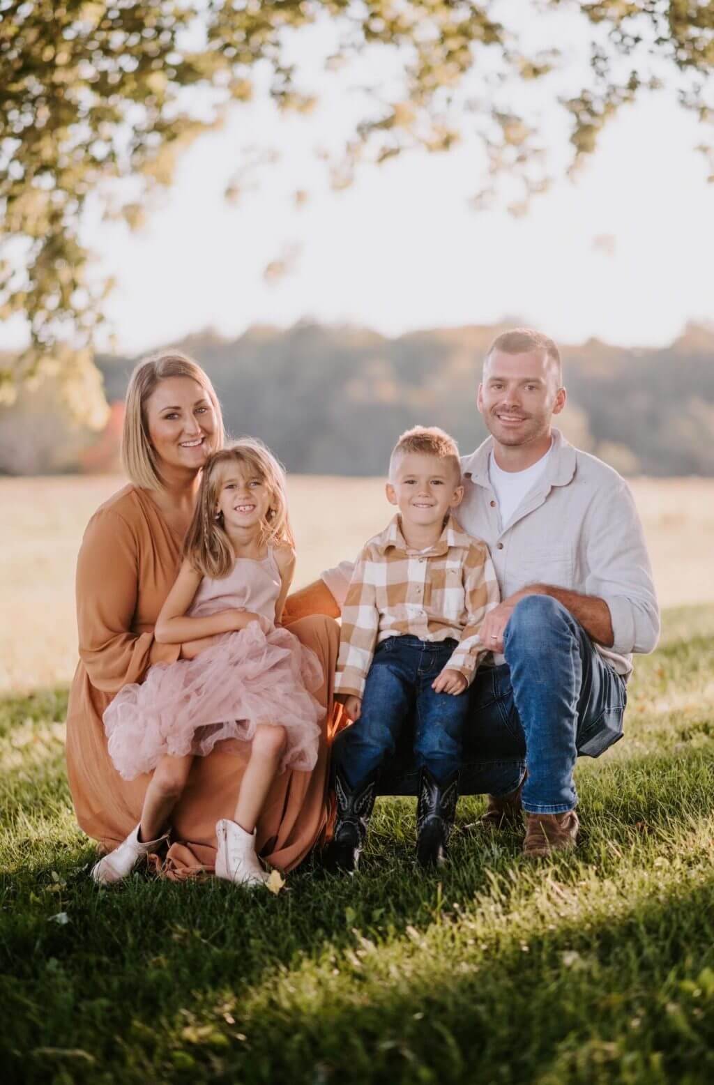 Family of four sitting together in golden field during sunset