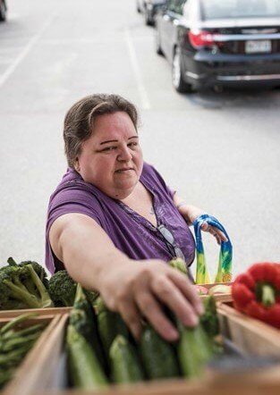Woman in purple top unloading fresh vegetables from colorful shopping bag