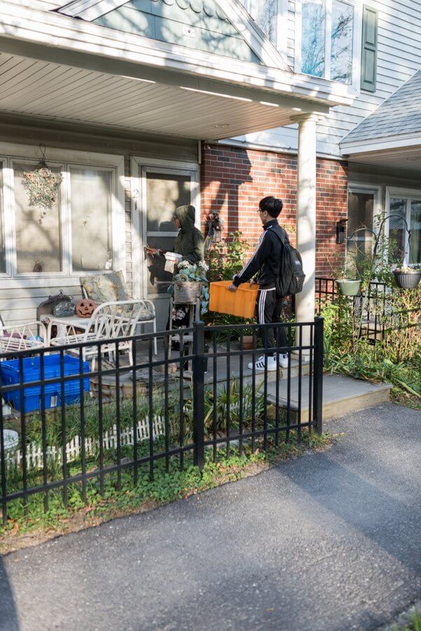 Two people standing near fence in front of brick house with potted plants