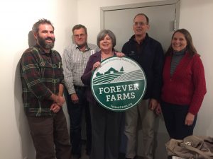 Five people posing with Forever Farms logo sign in office setting