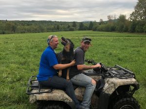 Two people riding an ATV together in a green rural field landscape
