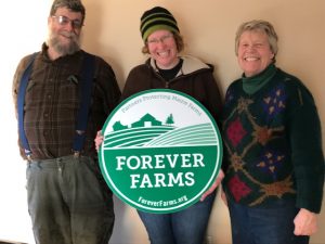 Three farmers pose with a Forever Farms green logo sign