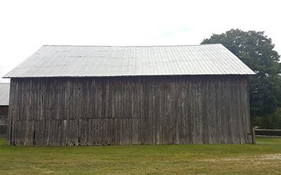 Old weathered wooden barn with metal roof in grassy rural field