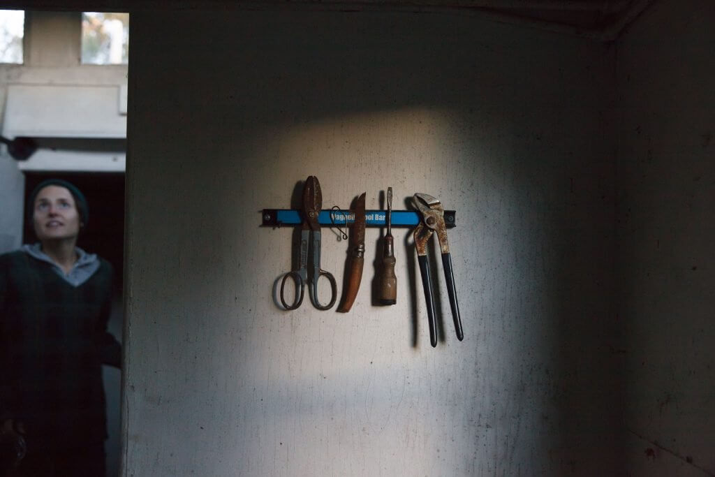 Old rusty tools hanging on blue magnetic bar against textured wall