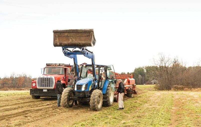 Farmers with blue tractor, red truck, and farming equipment in autumn field