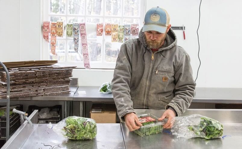 Worker in Carhartt jacket prepares fresh produce in commercial kitchen