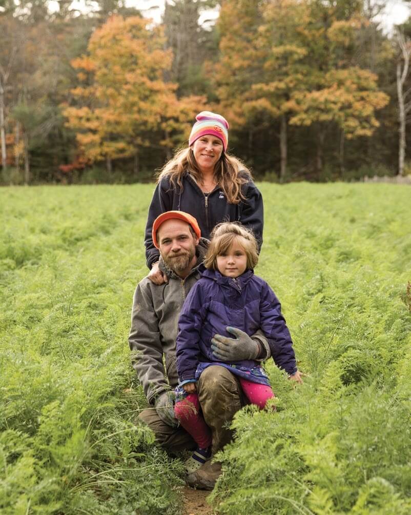 Family of three sitting together in autumn field with colorful trees