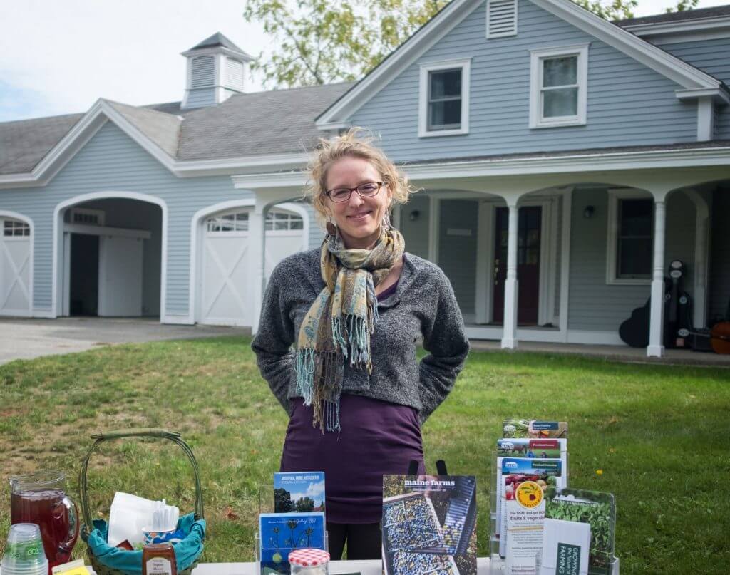Woman in scarf standing in front of house with gardening and farm materials