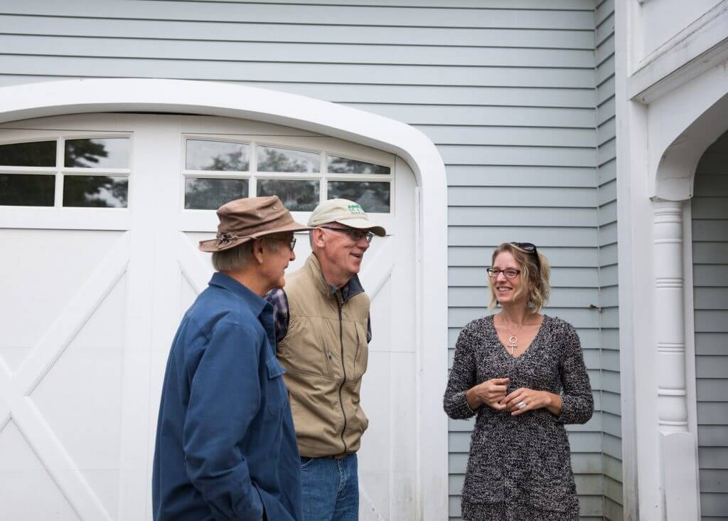 Three people talking outside white garage door on residential building