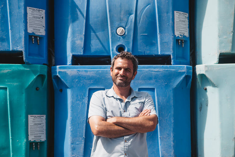 Smiling worker standing confidently in front of blue industrial containers