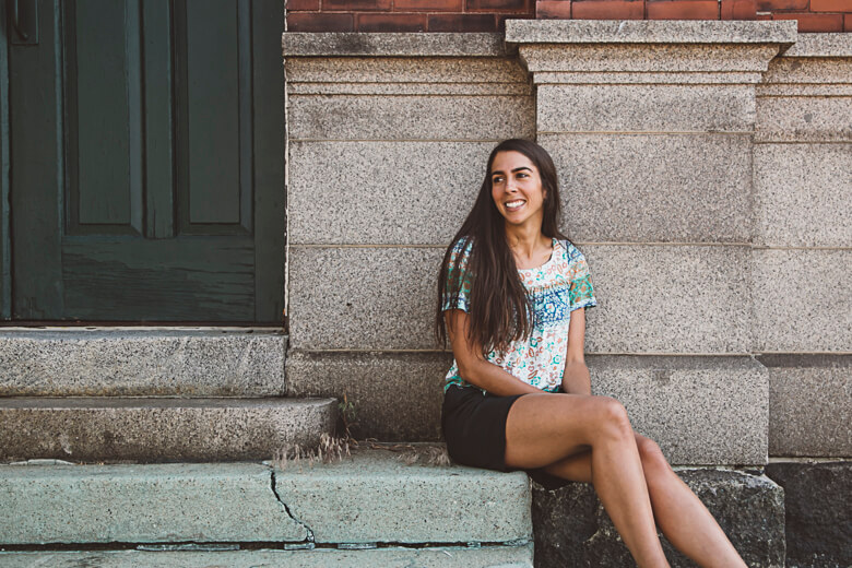Smiling woman sitting on stone steps wearing floral top and black shorts