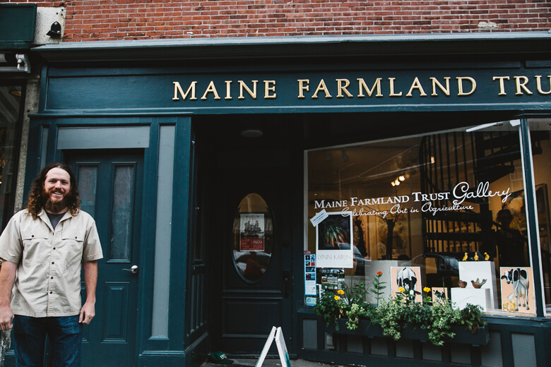 Man standing outside Maine Farmland Trust Gallery with storefront display