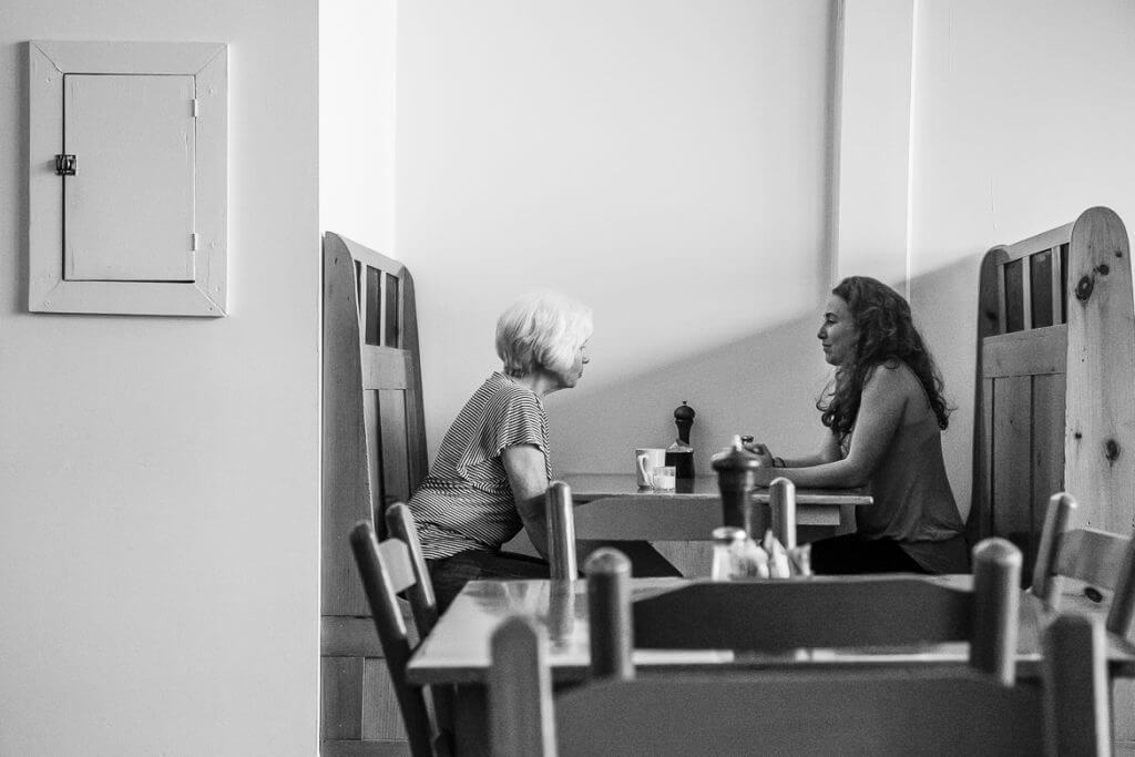 Two women having conversation at cafe table with coffee and accessories