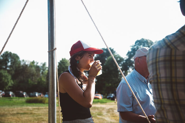 Person in red cap drinking from cup at outdoor event with others
