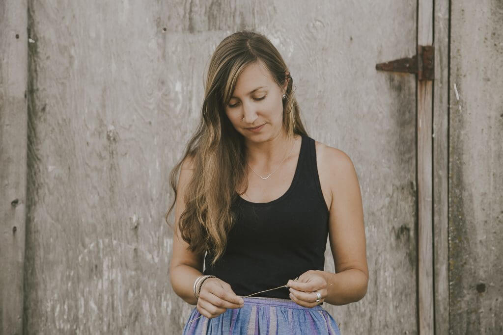Woman in black tank top standing by wooden wall, looking down thoughtfully