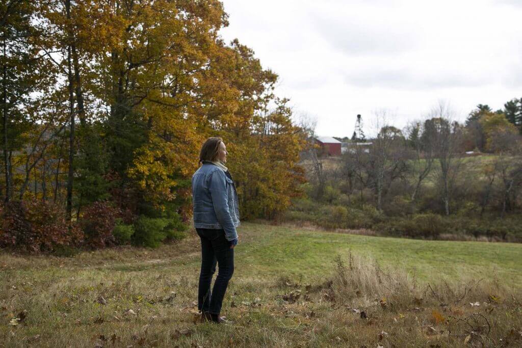 Person standing in autumn field with trees and red barn in background