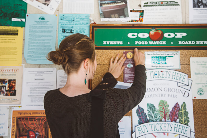 Person checking community bulletin board with Co-op events and ticket information