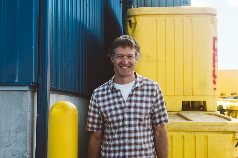 Smiling person in plaid shirt standing near yellow and blue containers