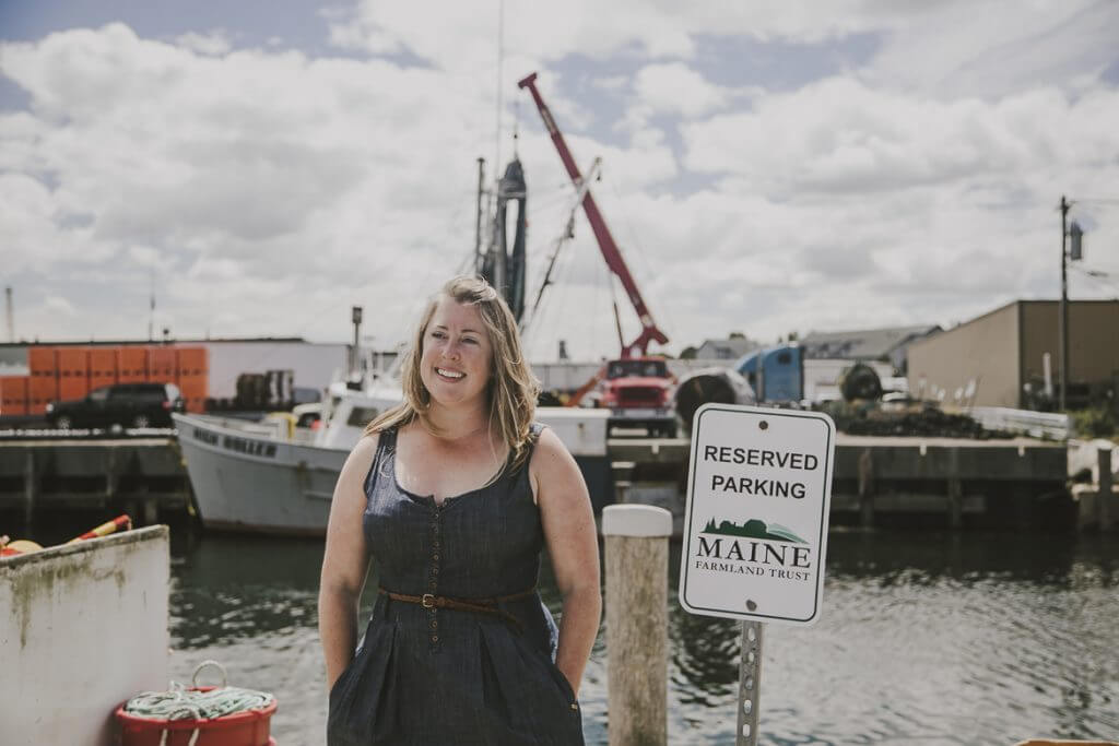 Smiling woman at Maine harbor with fishing boats and reserved parking sign
