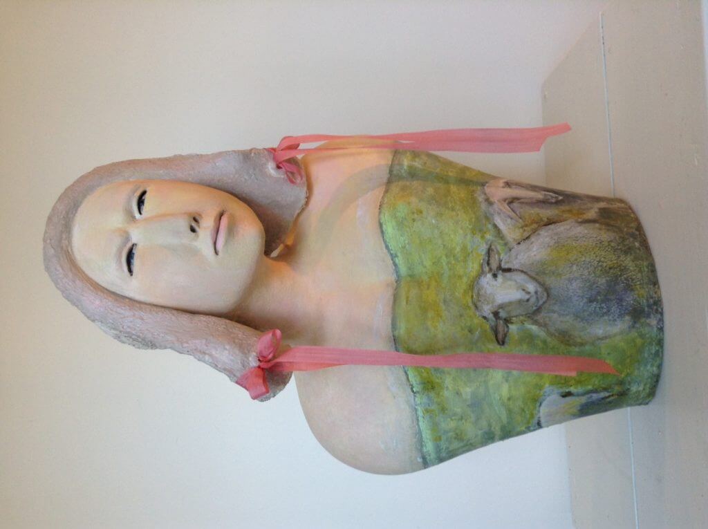 Ceramic sculpture of serene figure with ribbons and green-yellow background
