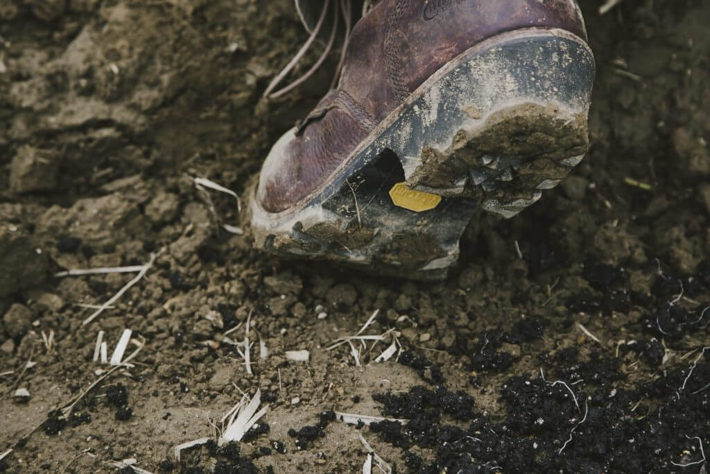 Muddy hiking boot with Vibram sole stepping on dirty ground