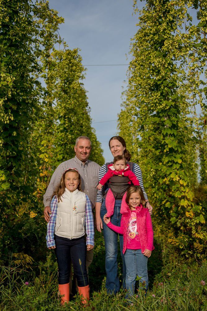Family of four posing together in lush green tree-lined outdoor setting