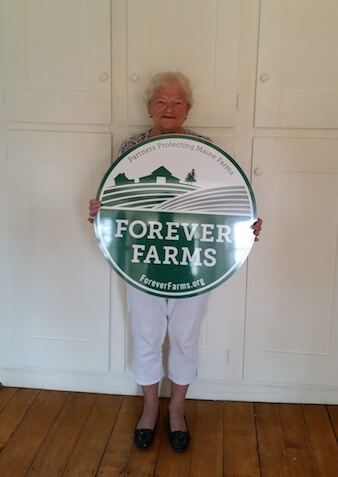 Older person holding large green Forever Farms circular logo sign