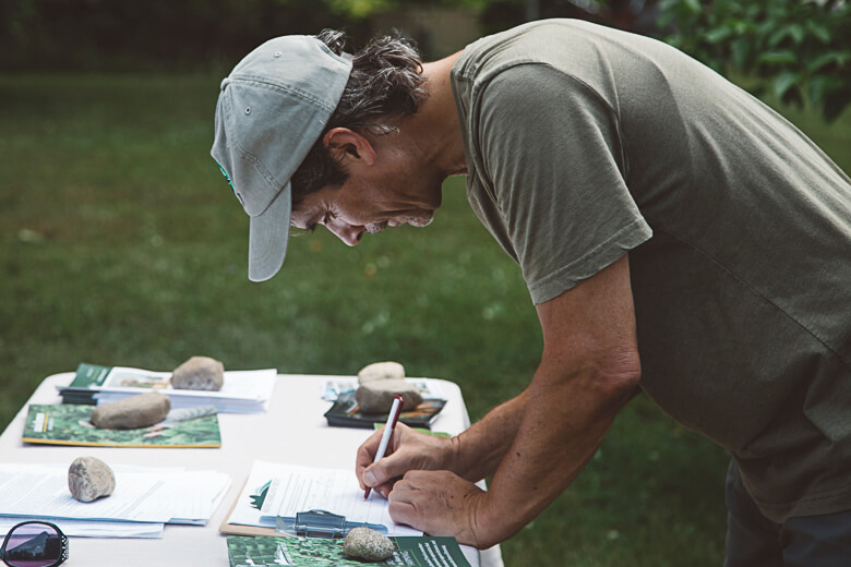 Person in cap studying documents and rocks outdoors at a table