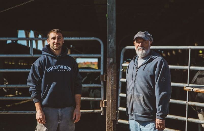 Two men in hoodies standing together near metal gates in rustic setting