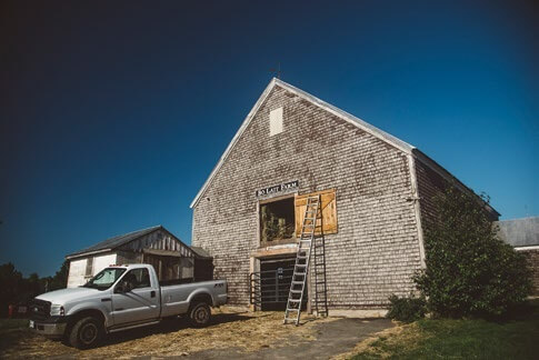 Weathered wooden barn with pickup truck and ladder on sunny day