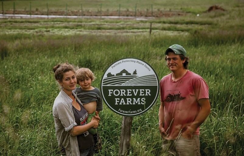Family standing by Forever Farms sign in grassy field