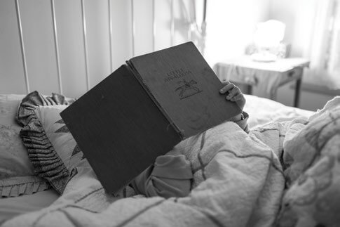 Black and white image of someone reading a book in bed