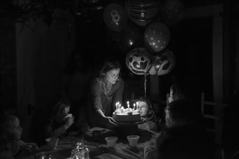 Child blowing out birthday candles with family in dimly lit room
