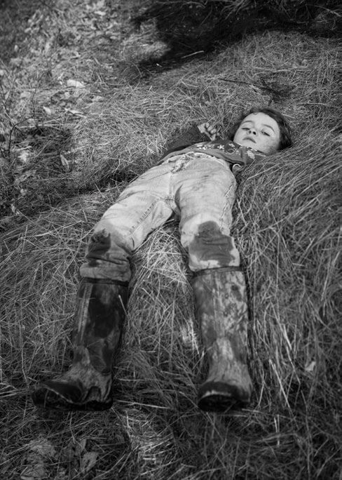 Child lying in grass wearing oversized boots, looking peaceful