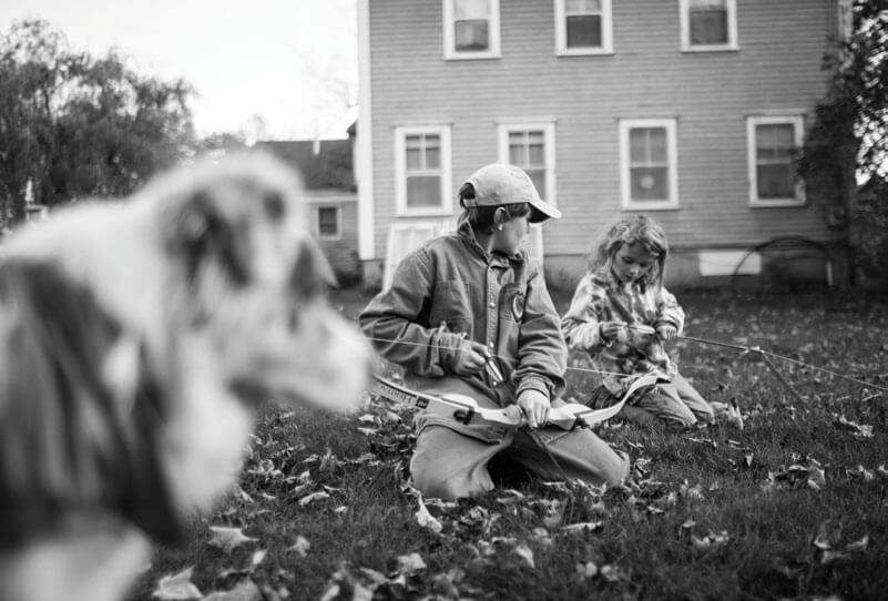 Child and adult read together on lawn with dog in foreground
