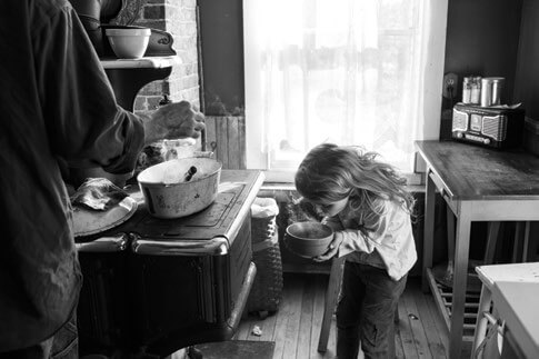 Child and parent in rustic kitchen, black and white, cooking together