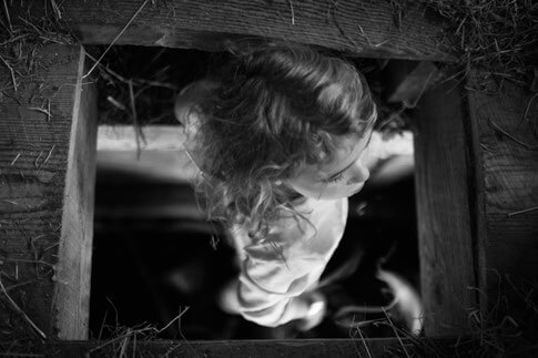Child peering through wooden window frame in dramatic black and white