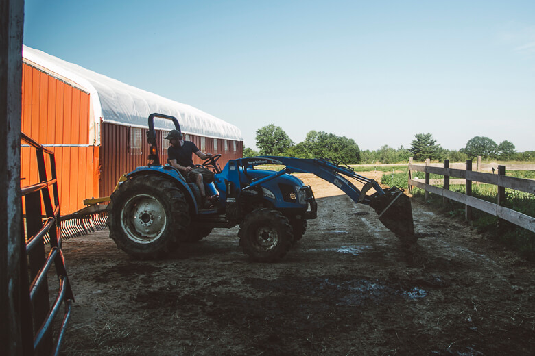 Blue tractor with loader near orange barn and wooden fence on farm