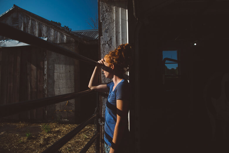 Person in blue shirt leaning against wooden fence near rustic building