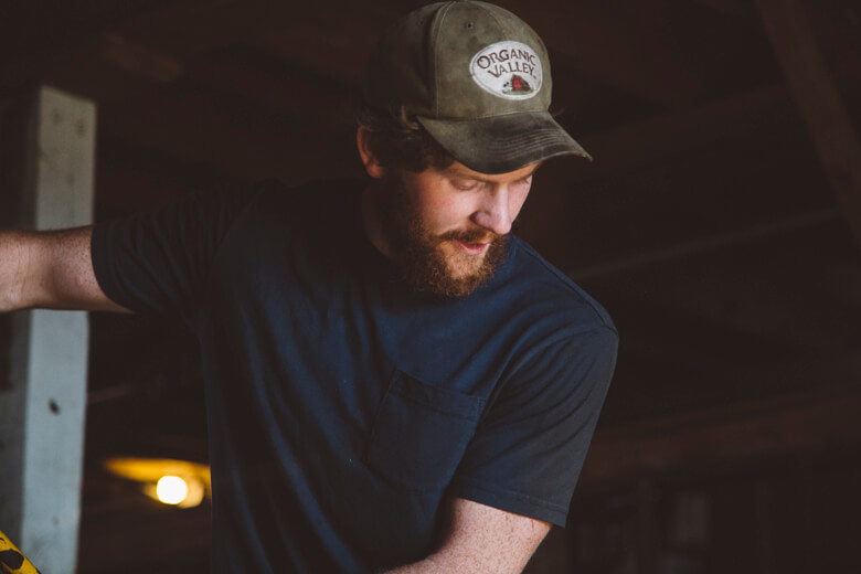 Bearded man in Organic Valley cap looking down in dimly lit setting