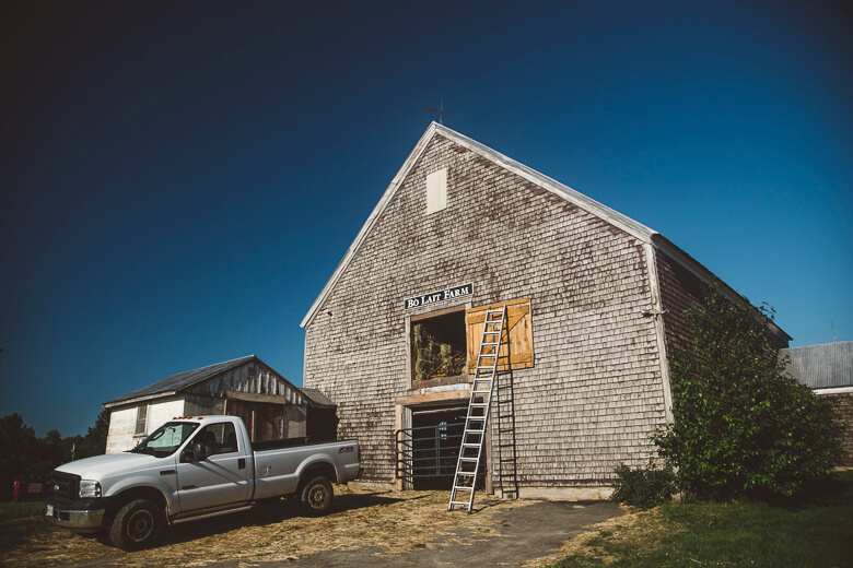 Weathered shingle barn with pickup truck and ladder on sunny day