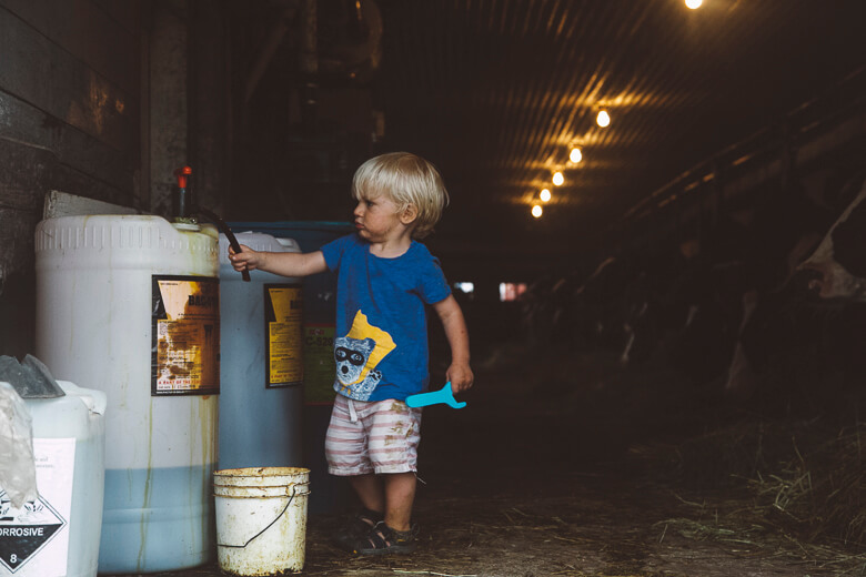 Young child in blue shirt exploring dimly lit storage area with chemical containers