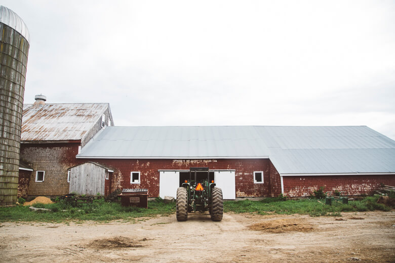 Old red barn with tractor and silo on rural farmyard in overcast weather